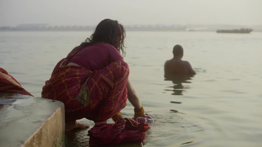 Woman washing clothes by the seaside with a man bathing in the foreground