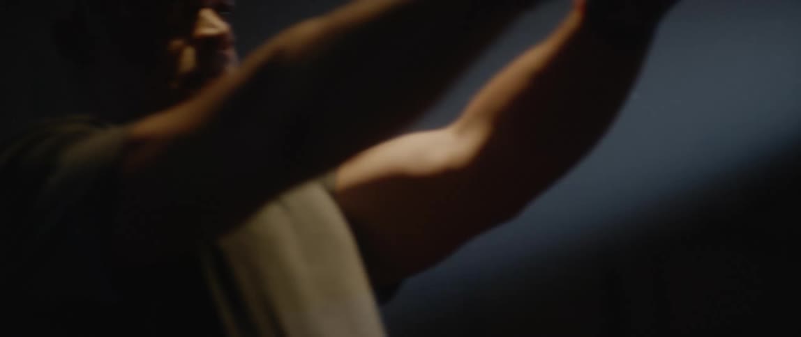 A man does front raises with dumbbells in a dark room