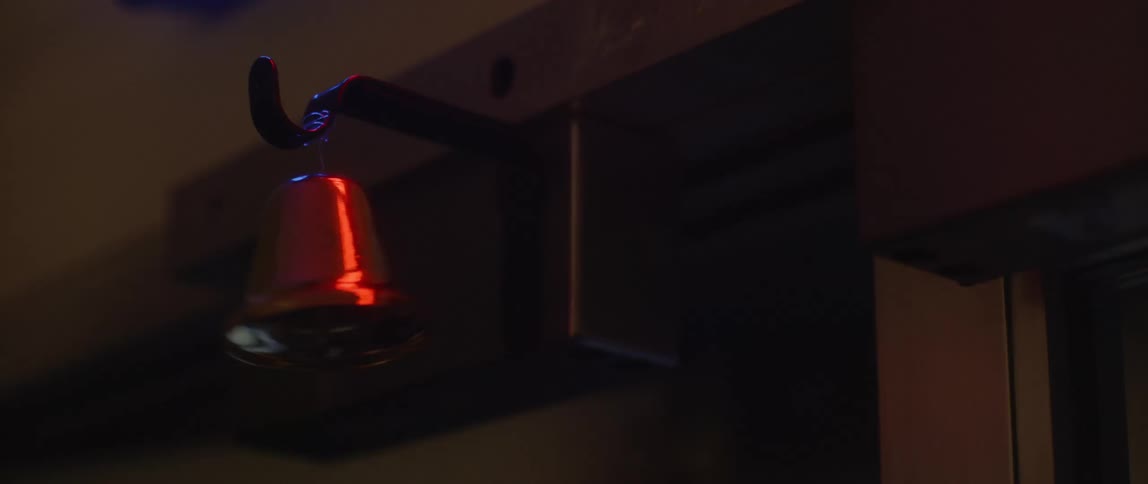 A copper bell hung above the top corner of a door swings back and forth when the door opens and closes