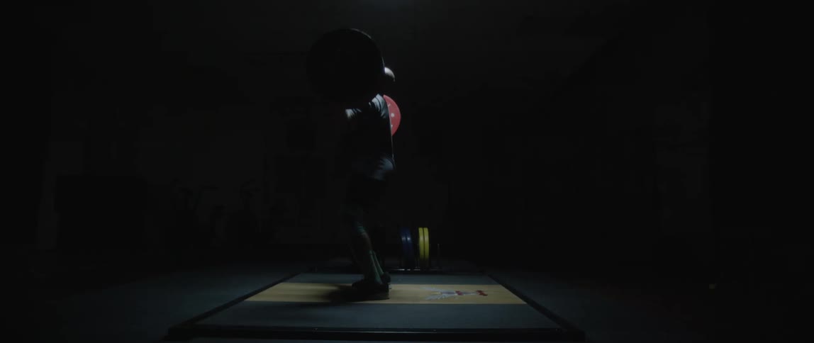 Man walking to the center of a dark room and performing a barbell weightlifting
