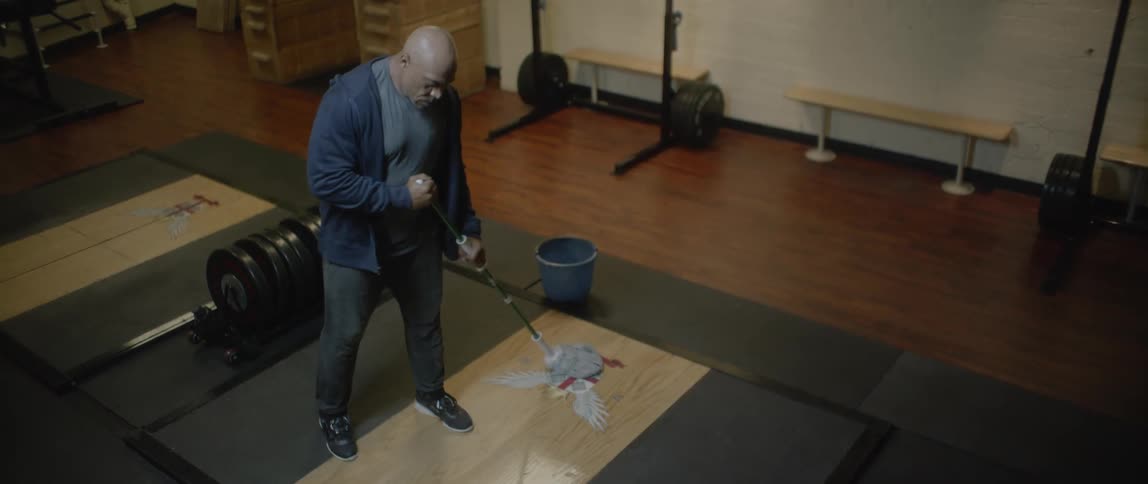 Man cleaning a wooden floor area in a gym