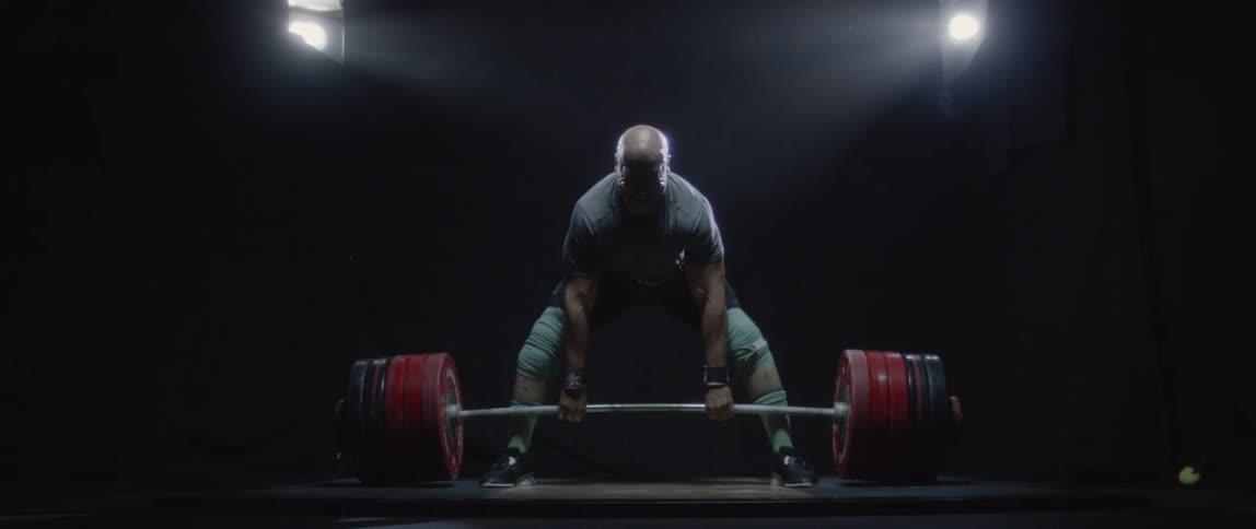 Man performing a barbell lift in a dark room