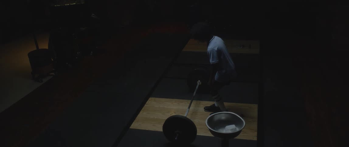 Boy walking and squatting in front of a free weight bar with weights