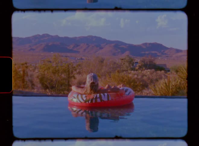 Woman lying on a float in the pool facing a natural landscape with mountains on the horizon