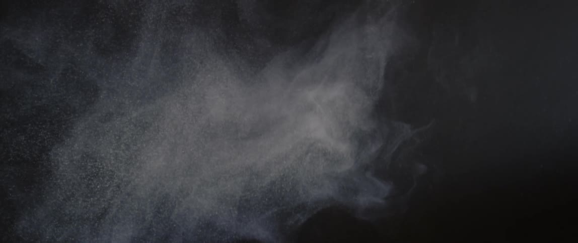 Small white smoke particles swirl and begin to dissipate against a dark background