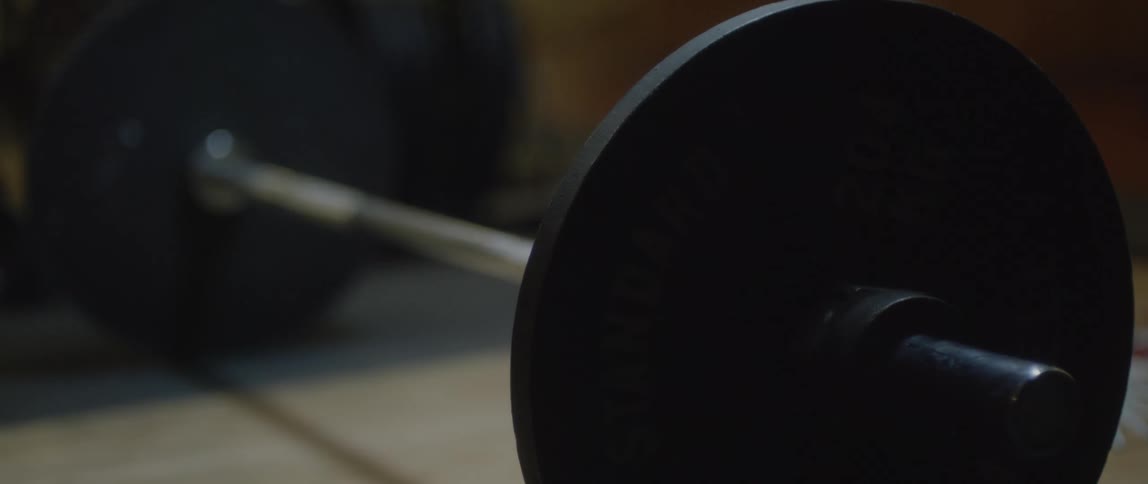 A barbell with a single weight on both ends sits on a gym floor