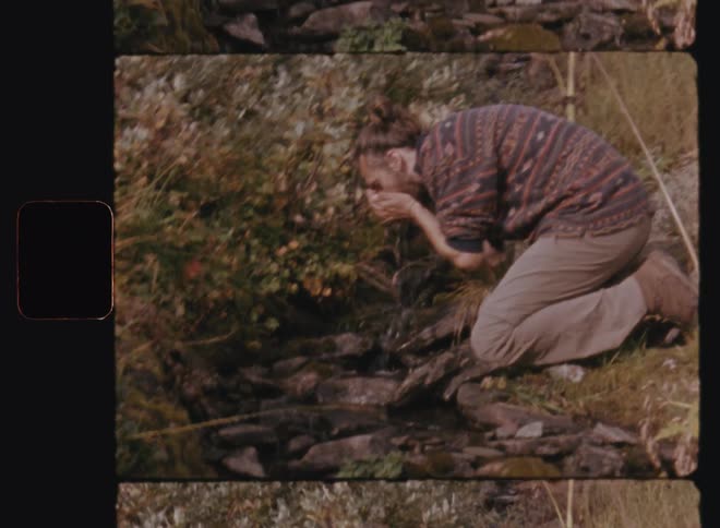 A man in a jungle drinking water from a stream