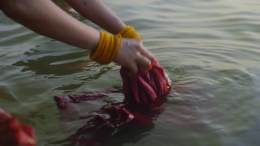 Hands of a woman washing clothes by the riverbank