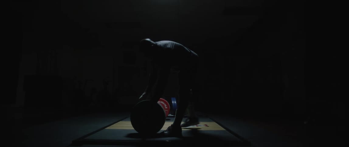 Man placing protective equipment next to weight plates on a barbell in a darkroom