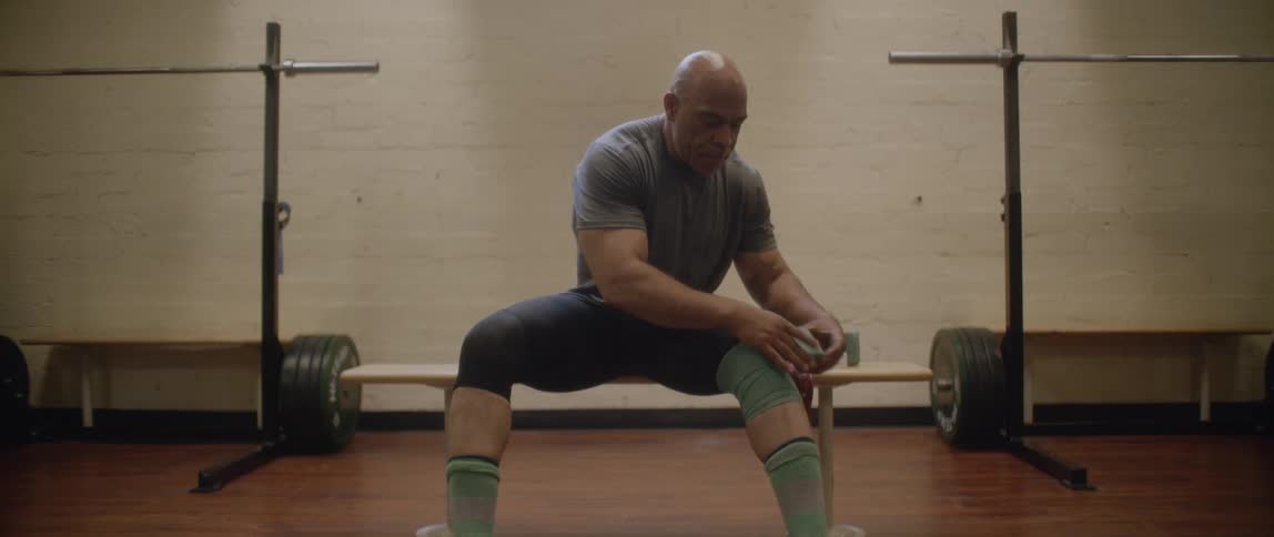 Man sitting and wrapping a bandage around his knee in a gym