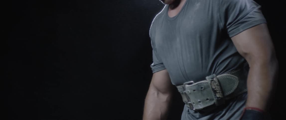 A strong man squats and stands up and there is a strong light behind him in a dark environment