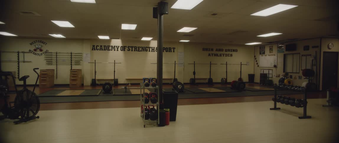 The panel ceiling lights of a basement gym weight room turn on a couple at a time until they are all lit