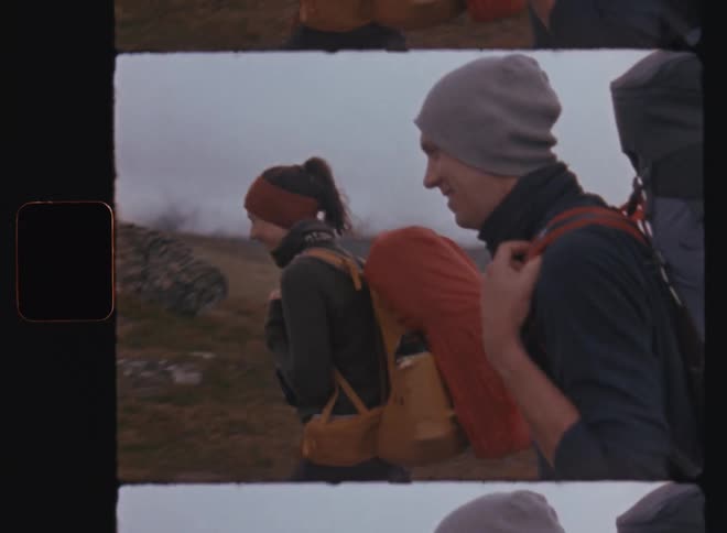 A male and a female hiker each with backpacks trek across the plains under a sky filled with clouds