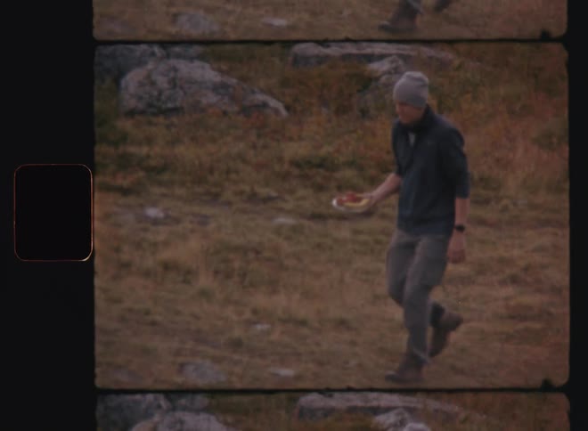 A man with a cap walking on a lawn with some stones