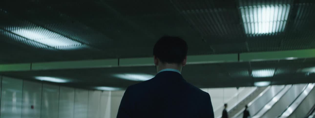 Man in a suit walking towards an escalator with his back turned