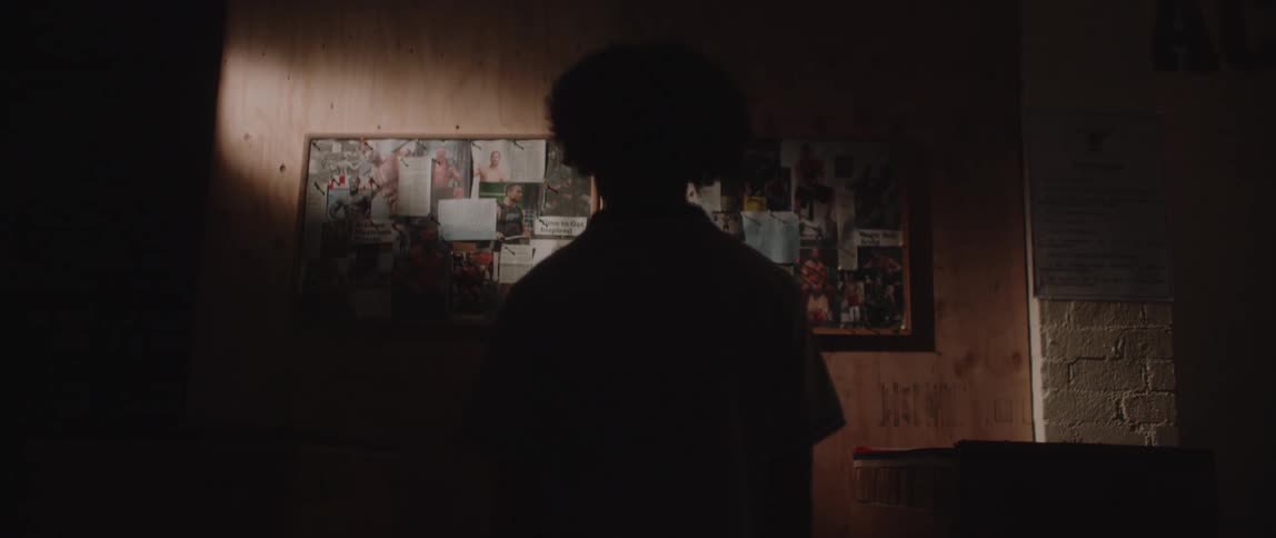 A boy looks at pictures and cutout newspaper articles on two bulletin boards in a dark room