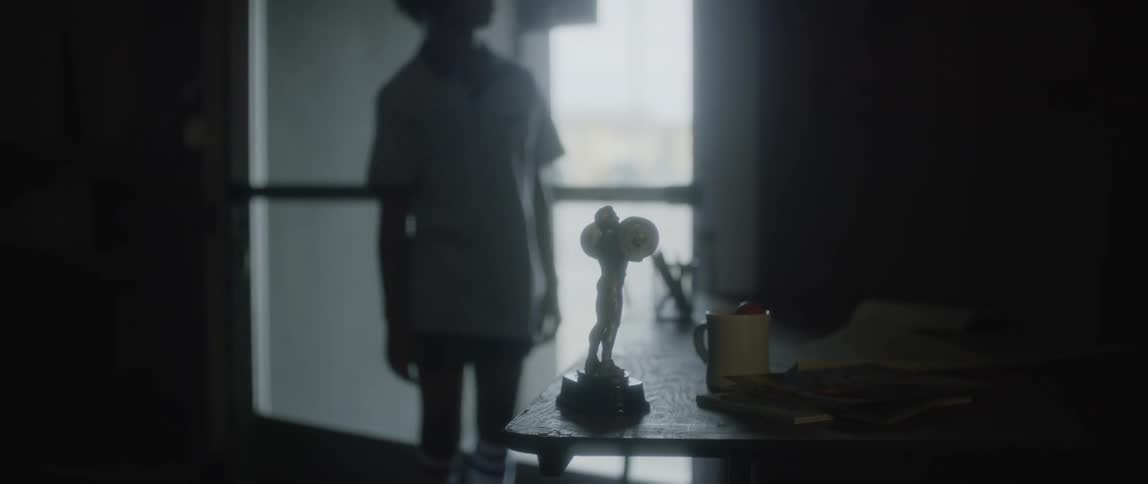 Skateboarder props skateboard near door after entering room then examines statuette