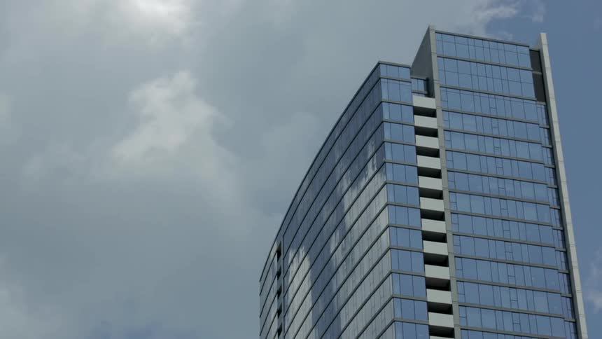 A tall building is reflecting the moving clouds above
