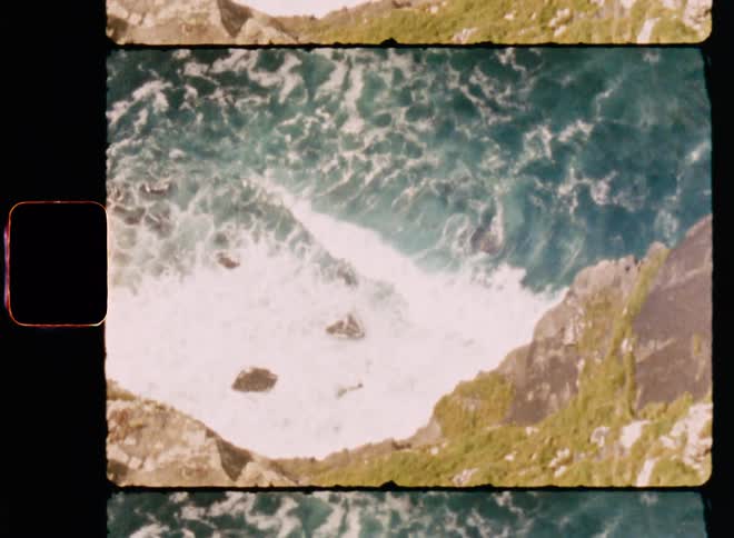 Waves break and foam at the base of a steep oceanside cliff