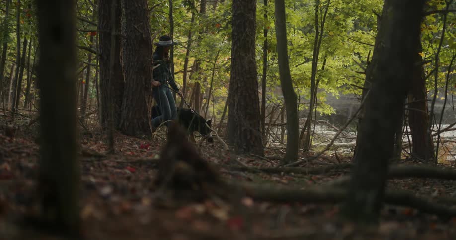A woman walking a dog through the forest during the day