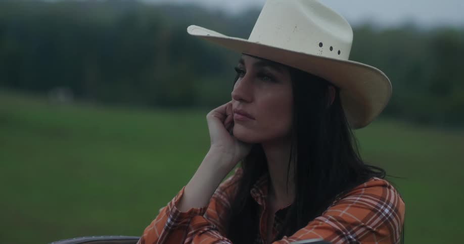 Woman with a cowboy hat resting her head on her hand looking around in a vast open field