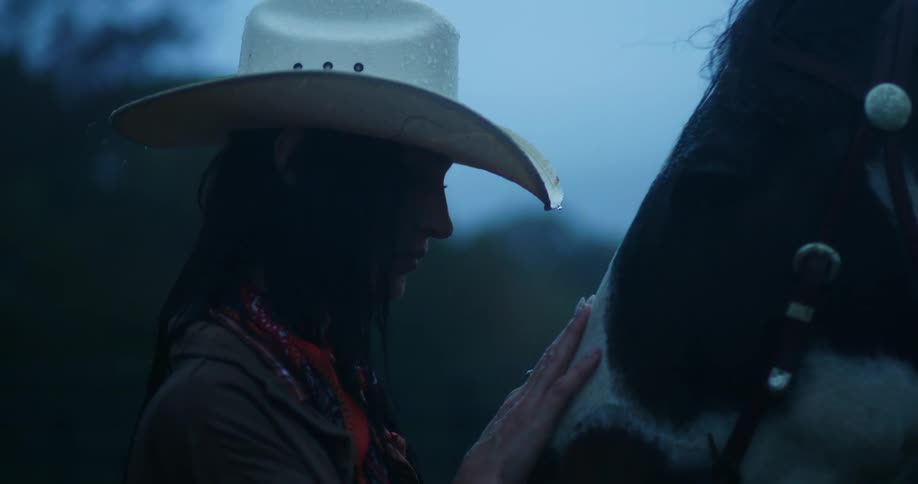 Cowgirl caressing the horses face on a rainy day