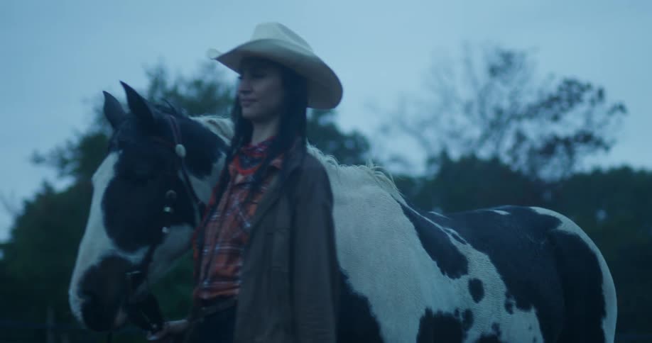 A woman in a cowboy hat walks along a horse