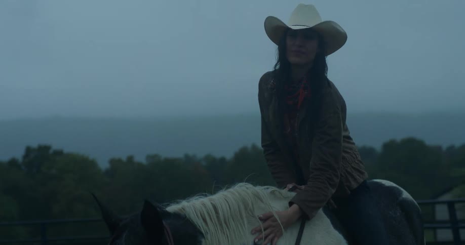 Cowgirl on top of the horse petting it under the morning sky