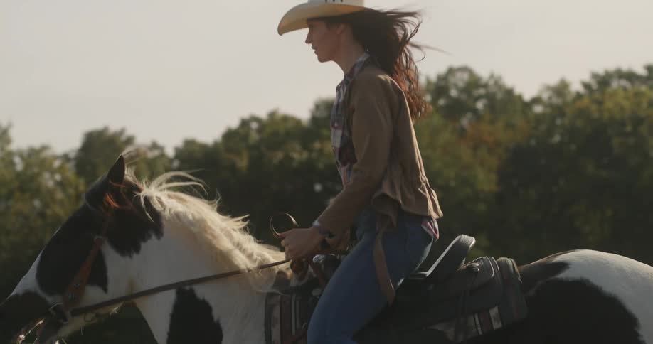 A woman in a hat riding a horse and her hair keeps moving