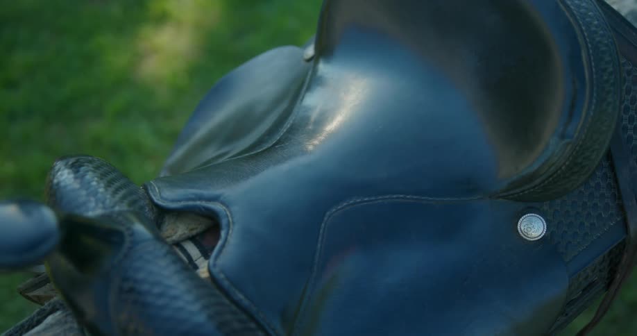 A black leather saddle on top of the wooden fence