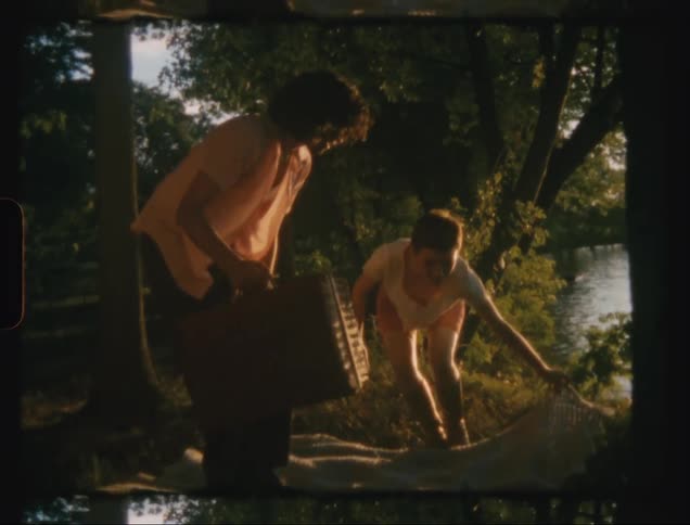 Man and woman sits on a laid down cloth near a river during the day