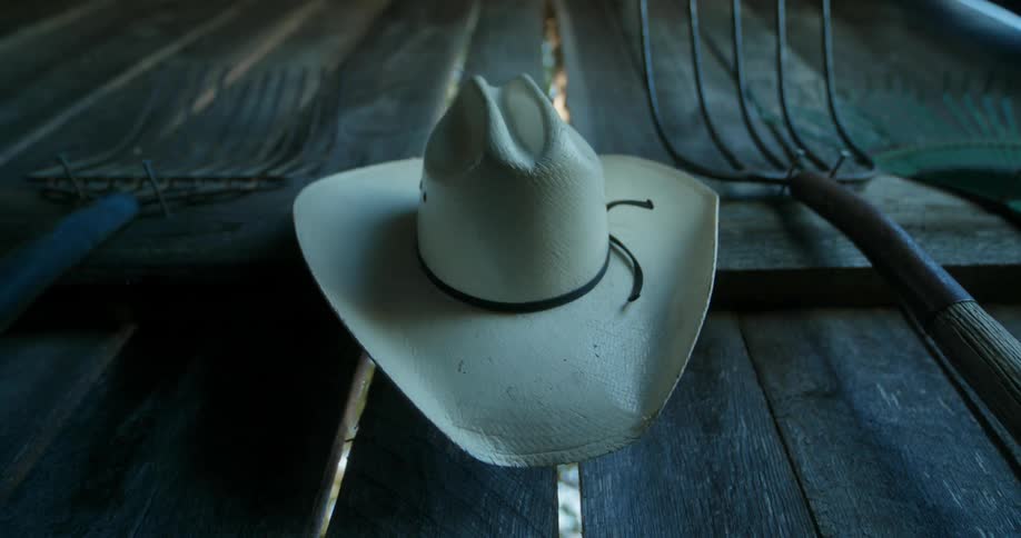 A person hanging a hat on a wall next to some pitch forks