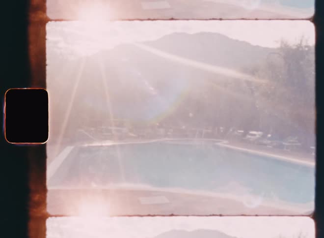 The sun is brightly shining down on the pool that is surrounded by trees and cars