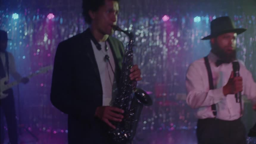 Smiling grayhaired woman standing in front of the stage while a band is playing in a nightclub with musicians playing instruments including a saxophone