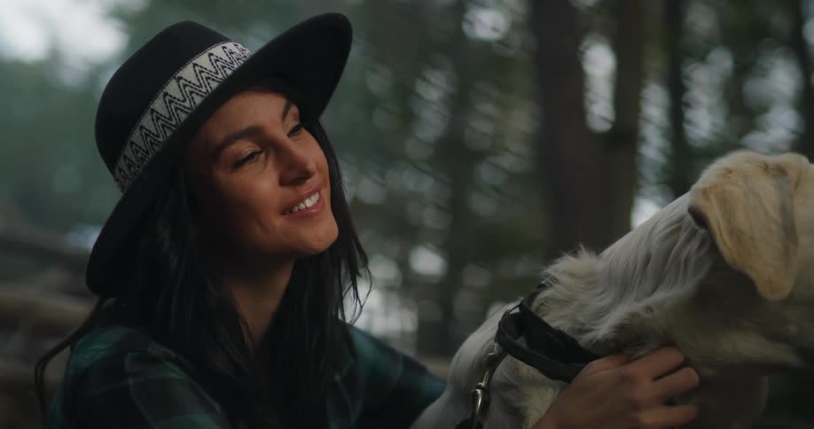 A woman smiles while a dog that is beside her receiving affection from her looks at her