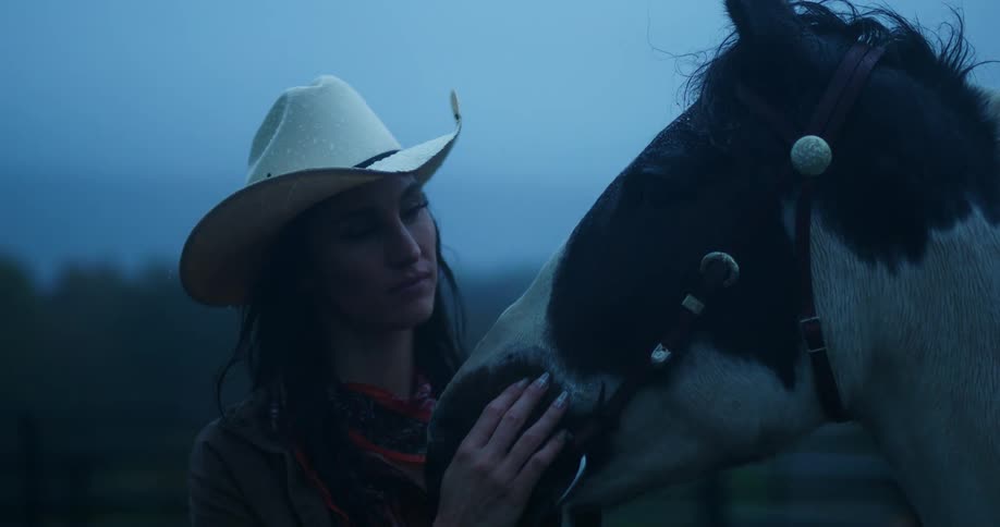 A woman in a hat is stroking a horse in front of her