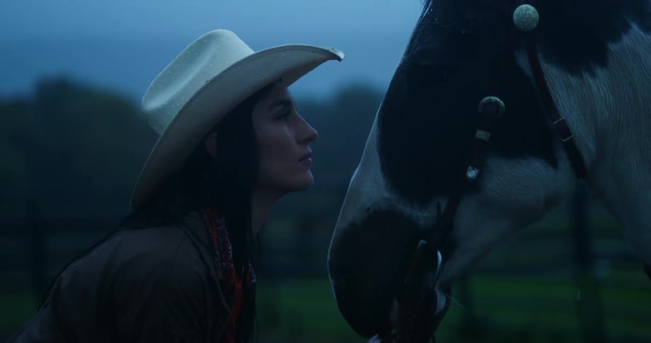 A woman in a cowboy hat is looking face to face with a horse