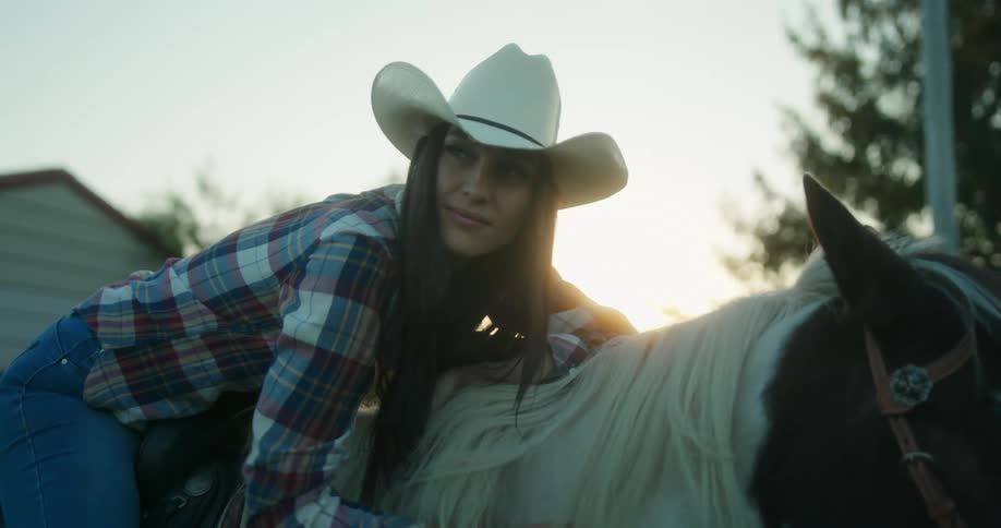 Lady rubs horses neck while sitting on it at sunset