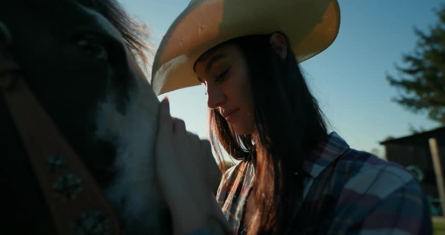 Woman in a cowboy hat affectionately touching the face of a horse with a clear blue sky in the background