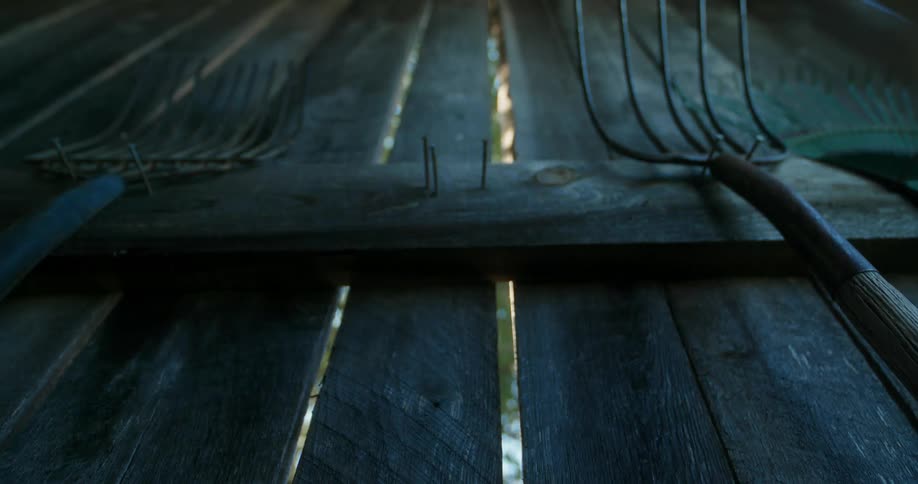 A cowboy hat hangs on the wooden wall with farm tools next to it