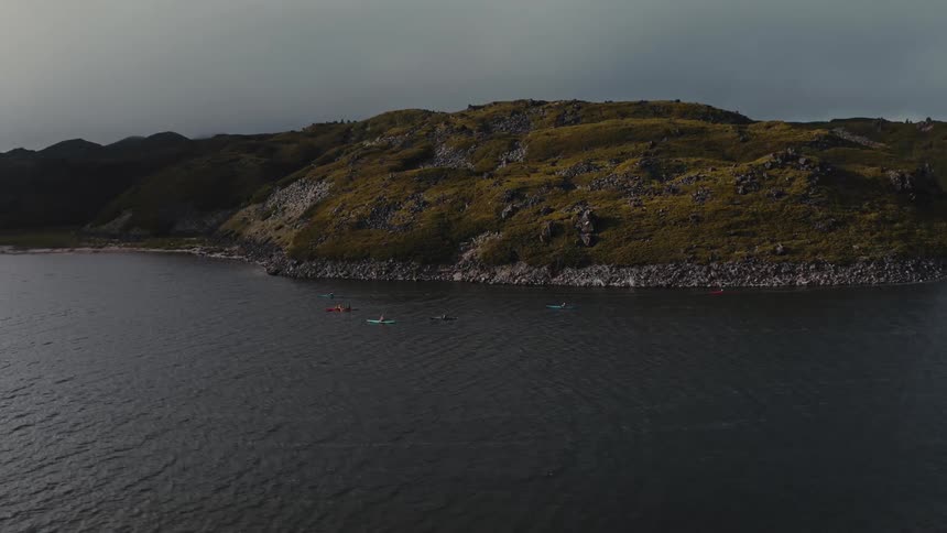 Aerial of the sea with people in canoes near the mountain coast