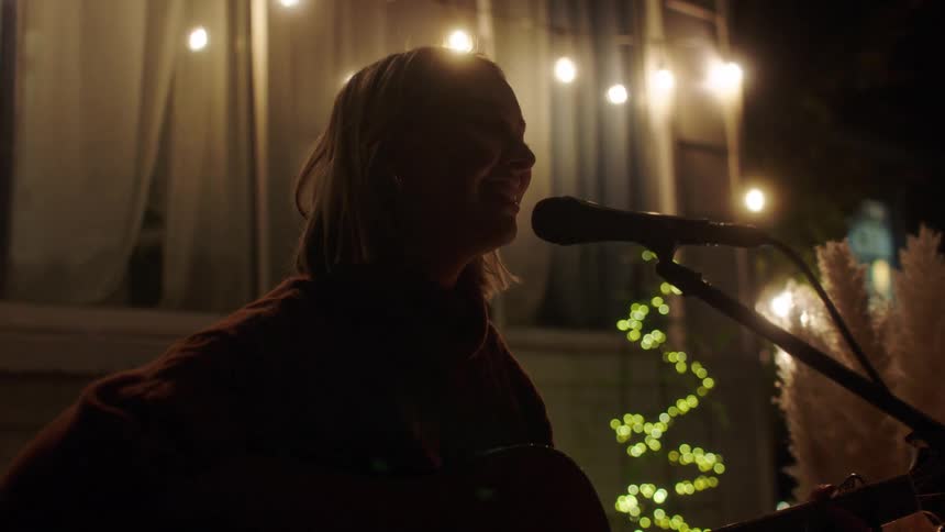 A woman singing and playing the guitar in a bright garden