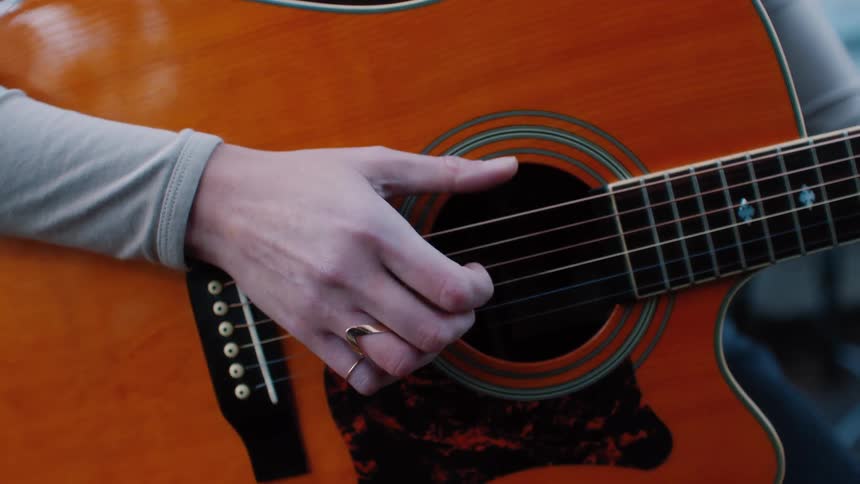 Blonde woman seated in front of a microphone playing the guitar
