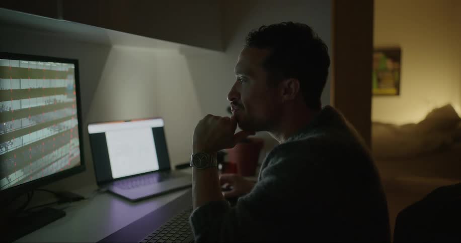 A man seated at his home desk diligently working on his laptop and monitor