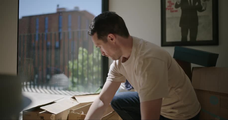 A man unpacking kitchenware from cardboard boxes on the floor