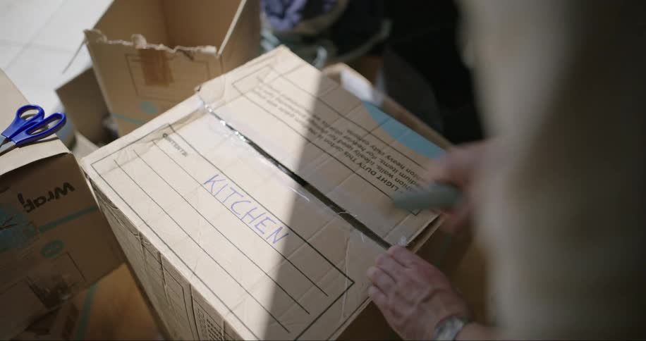 Person uses utility knife to open moving box containing kitchen items