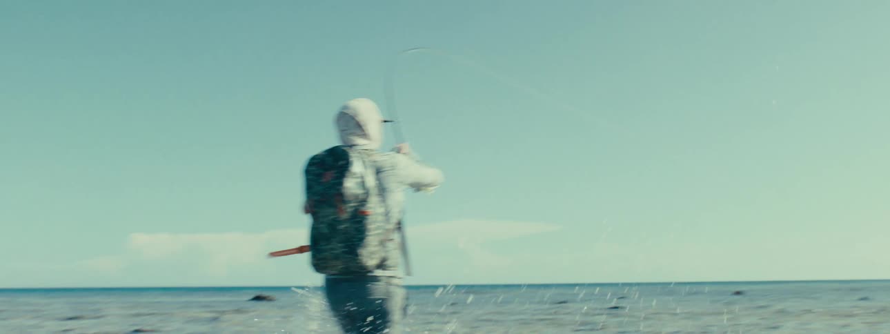 A man running in the ocean with the water by his ankles holding up a fishing rod