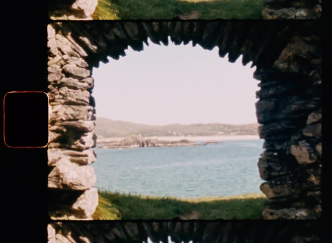 A stone arch frames the view of the water and the beach on the other side of it