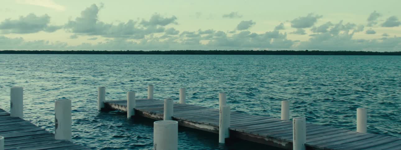A wooden pier extends over the calm body of water with white poles