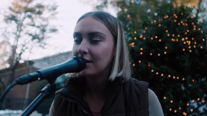 A young woman is playing with a device and singing into a microphone while sitting